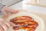 Spreading the pizza sauce on the prepared dough.' title='Sourdough Pizza Crust Recipe