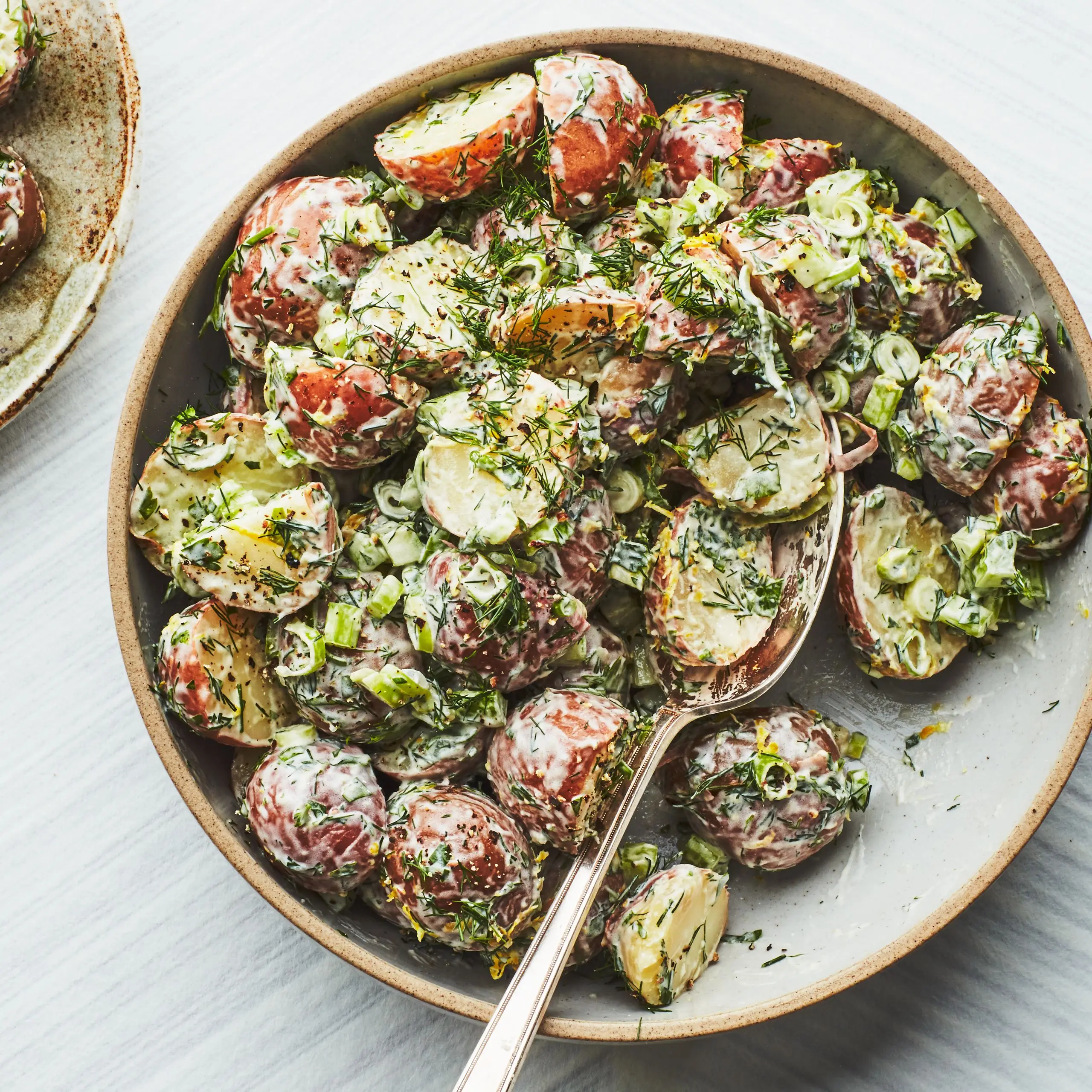 Photo of Creamy Potato Salad with Lemon and Fresh Herbs in a shallow bowl with a spoon and small side plate.