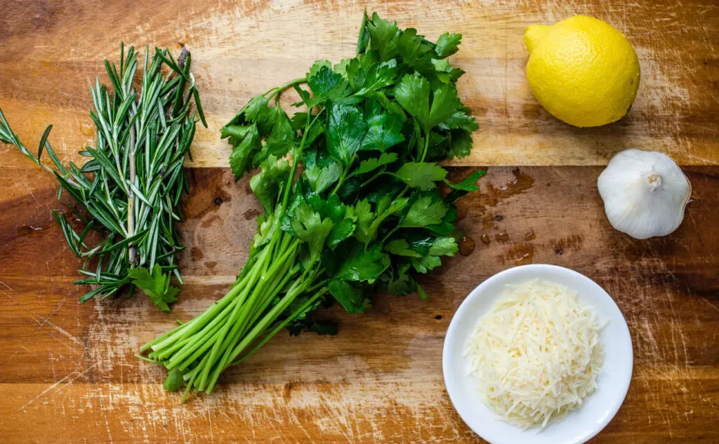 Fresh rosemary fresh parsley a lemon a garlic bulb and parmesan cheese on a cutting board.' title='Roasted Little Potato Recipe