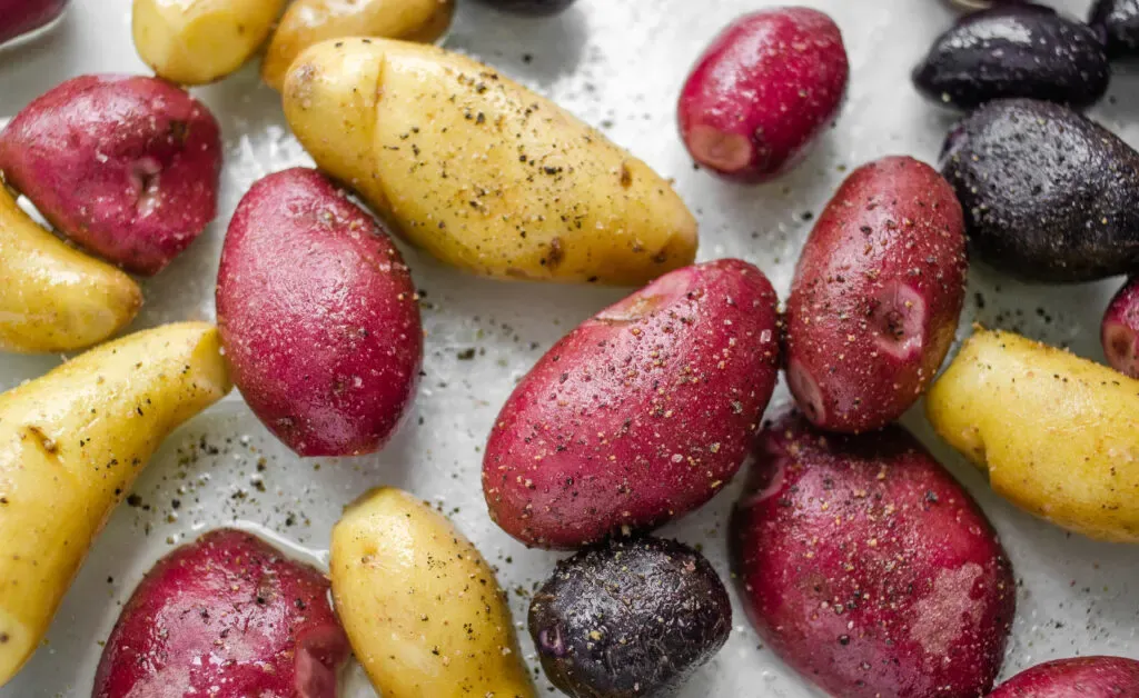Seasoning the mini potatoes with salt and pepper in the pan.' title='Roasted Little Potato Recipe