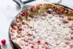 A raspberry clafoutis in a cast iron skillet with powdered sugar dusted on top.' title='Raspberry Clafoutis