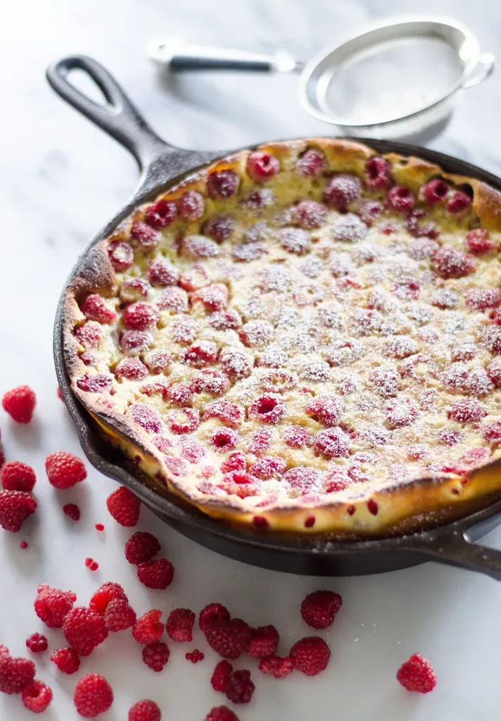 A Raspberry Clafoutis cooked in a cast iron skillet with a dusting of powdered sugar on top.' title='Raspberry Clafoutis