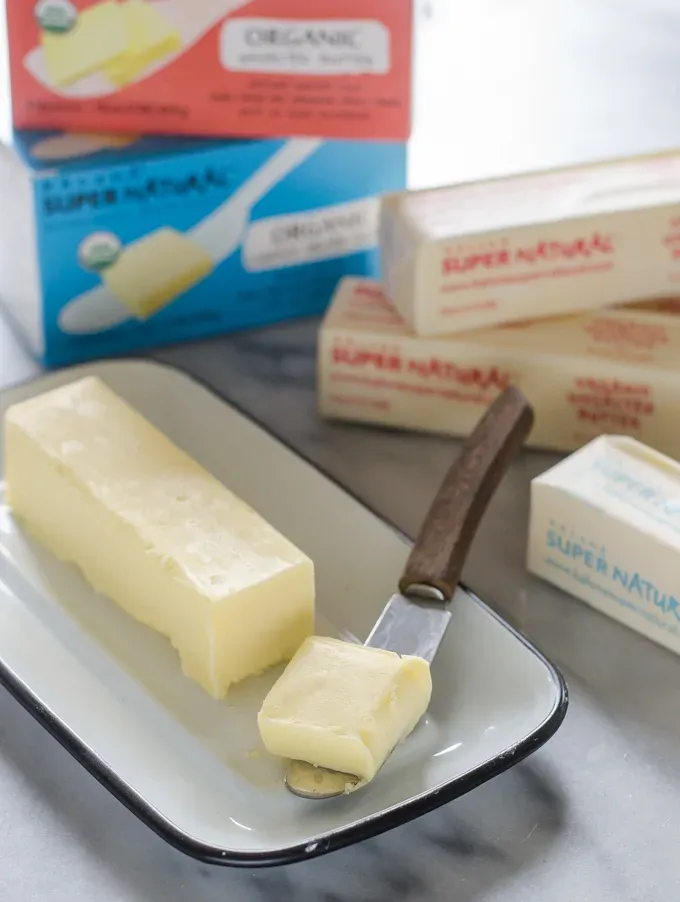 Butter in an enamel butter dish with a slice on a butter knife.' title='Ingredient Spotlight: Kalona SuperNatural Butter