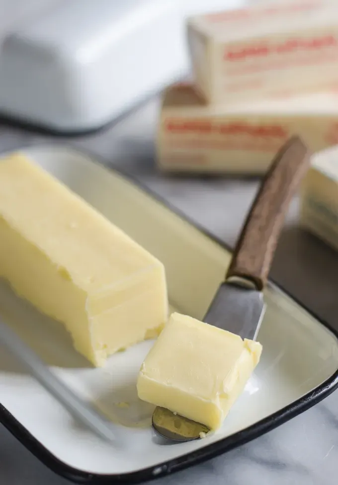 Butter in an enamel butter dish with a slice on a butter knife.' title='Ingredient Spotlight: Kalona SuperNatural Butter