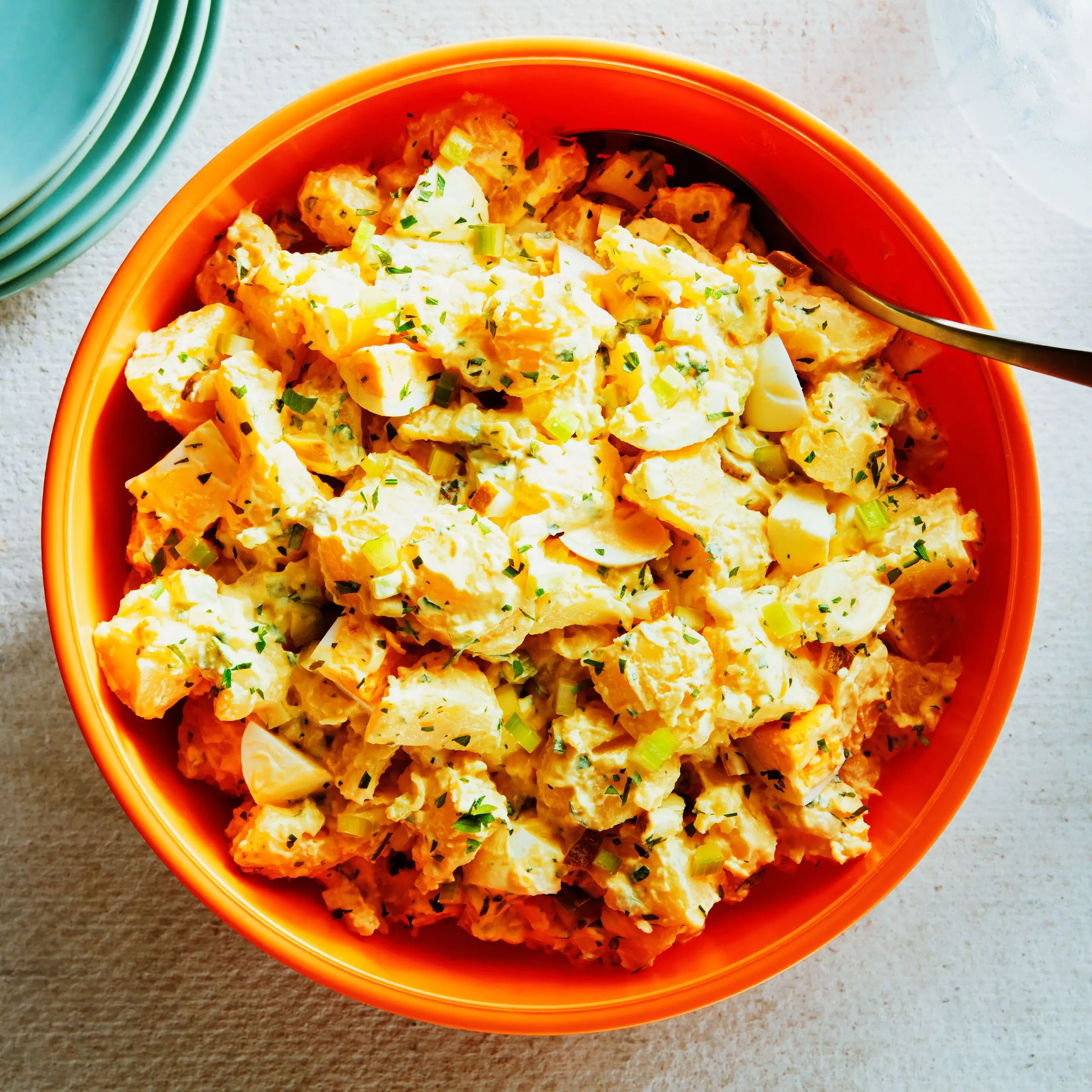 Cubed potatoes with hard boiled eggs chopped celery scallions chives and mayonnaise in a plastic bowl.