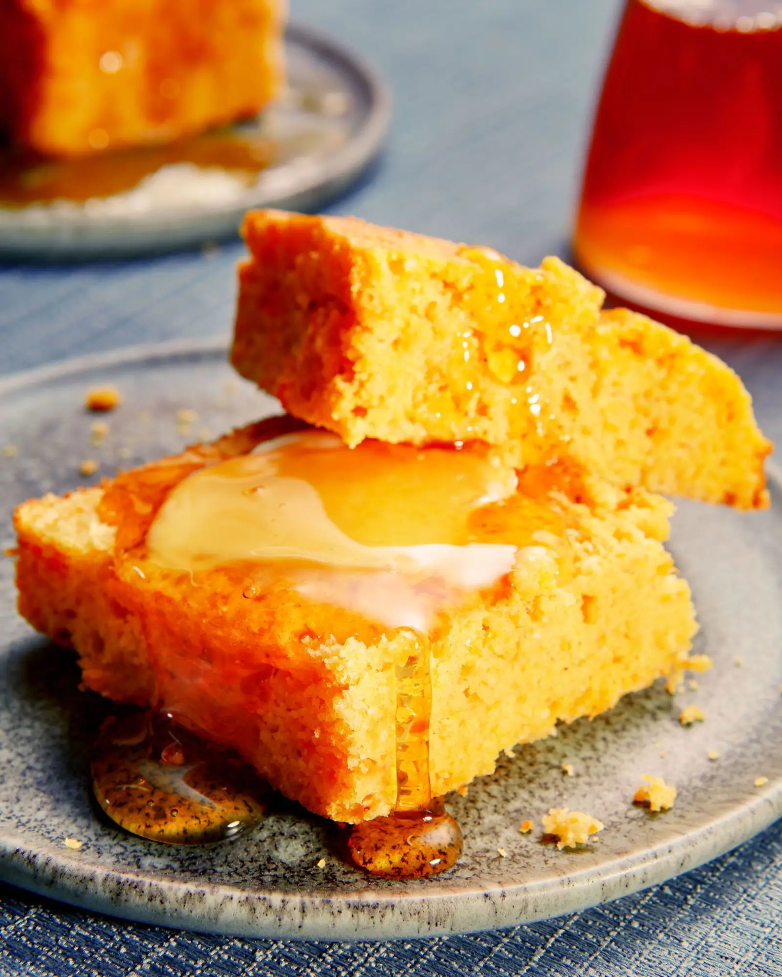 A slice of cornbread made with sweet potatoes cut in half on a plate served with honey and pats of butter.