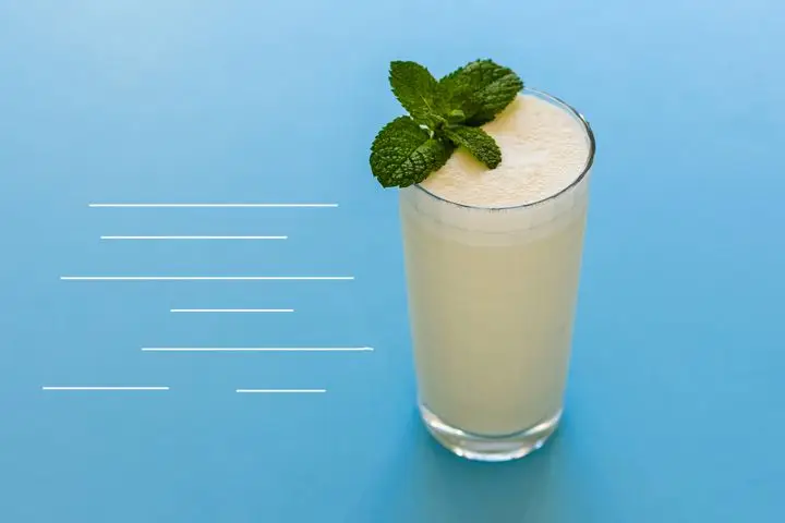A frothy, cream-colored Absinthe Suisse cocktail in a Collins glass garnished with fresh mint