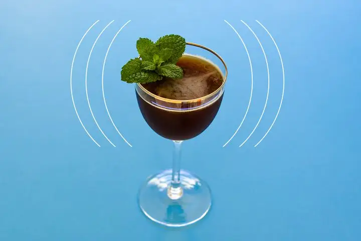 Death by Morning, a chocolate-brown shaken cocktail in a gold-rimmed Nick and Nora with a fresh mint garnish