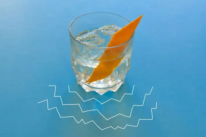 The clear Quill Riff cocktail, served on a large chunk of ice and garnished with a manicured orange twist