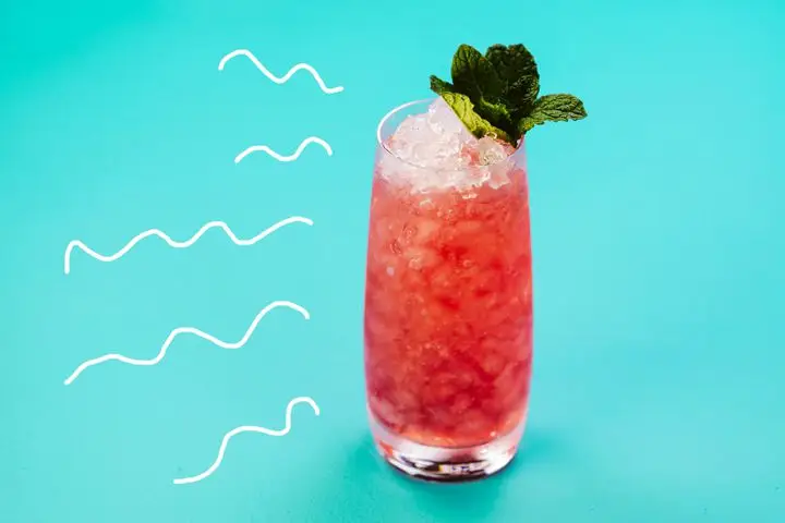 A thin, tapered Collins glass holds a bright red cocktail and bunch of crushed ice. It