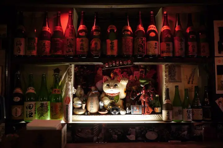 Dimly lit back bar lined with sake bottles at Sake Bar Decibel