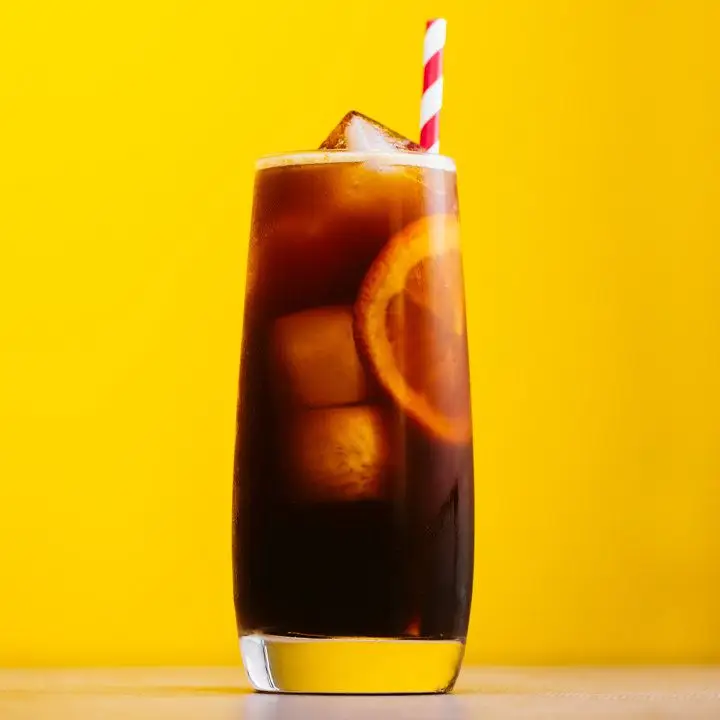 Jeez Louise highball cocktail with striped straw against yellow background