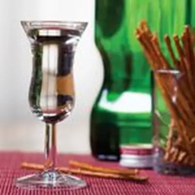 A stemmed tasting glass filled with genever in front of a cup of pretzel sticks
