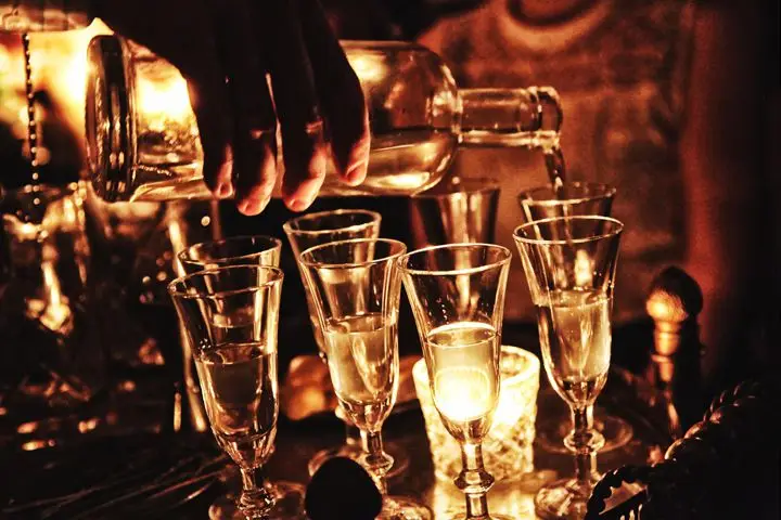 A dark, moody photo of a clear spirit being poured into cordial glasses