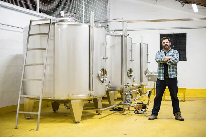 A man standing next to three large tanks in a warehouse with white walls and a yellow floor