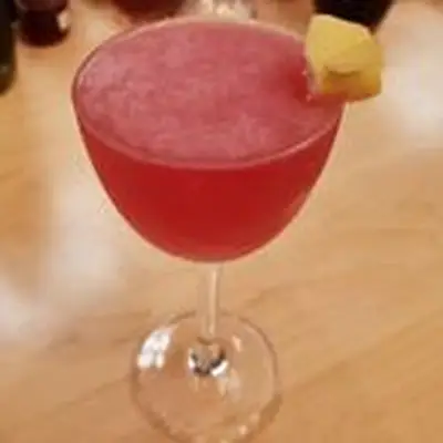 reddish-pink notro cocktail, served in a cocktail glass with a curled lemon peel garnish