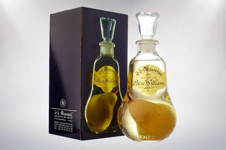 An elegantly curved bottle of clear pear eau-de-vie from G.E. Massenez, complete with a whole pear in it, sits next to a box with the bottle printed on it. 