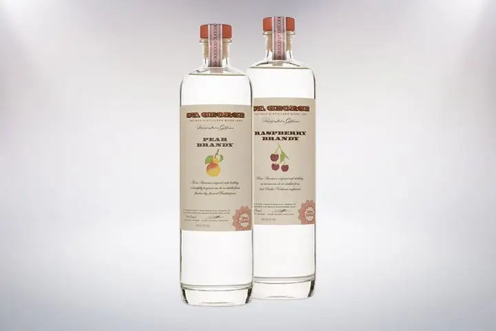 Two bottles from St George Spirits stand side-by-side on a blank background. The left bottle reads Pear Brandy, the one on the right reads Raspberry Brandy.