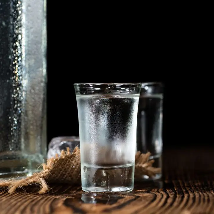 A single shot of soju, beaded with condensation, sits on a wooden table, a bit of burlap behind it