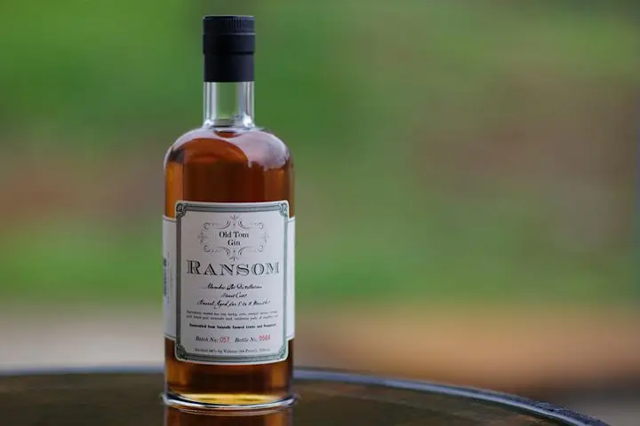 A bottle of amber-hued Ransom Old Tom Gin against a green outdoor background