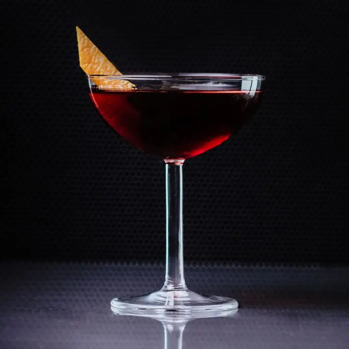 A Martinez cocktail in a coupe glass garnished with orange zest