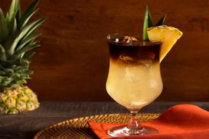 A Mai Tai in a clear stemmed glass with a black rum float and pineapple garnish