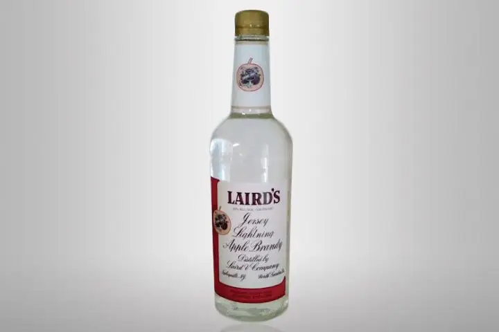 An empty bottle of Laird’s Apple Brandy, with a gold cap and white and red label, sits on a blank white background