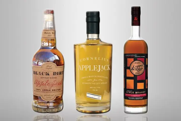 Three bottles of apple brandy sit on a blank background. From left to right, there’s Black Dirt Apple Jack, Cornelius Applejack, and Copper & Kings Apple Brandy
