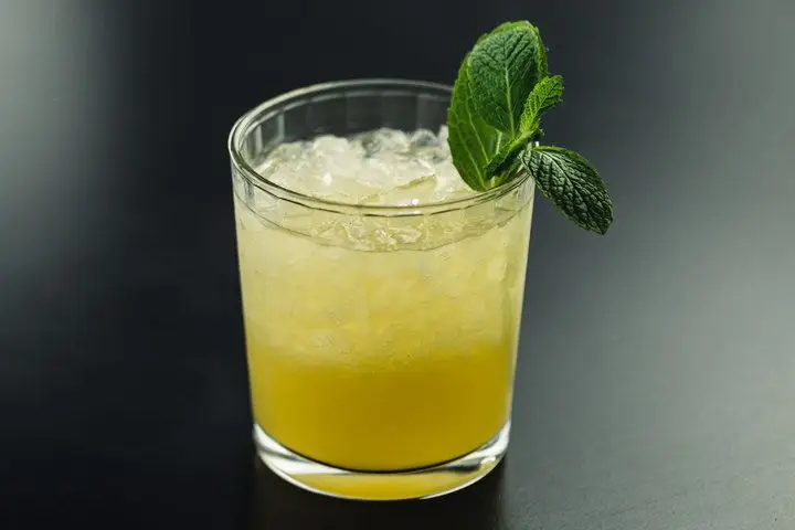 A golden-yellow Mai Tai on crushed ice in a beveled clear rocks glass and garnished with a fresh mint sprig