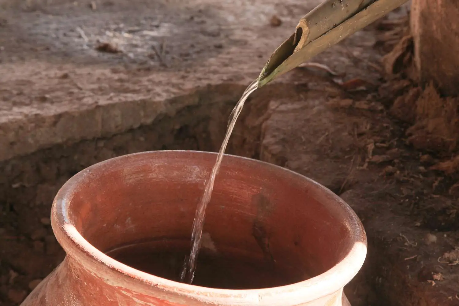 Spout pouring mezcal distillate into clay container