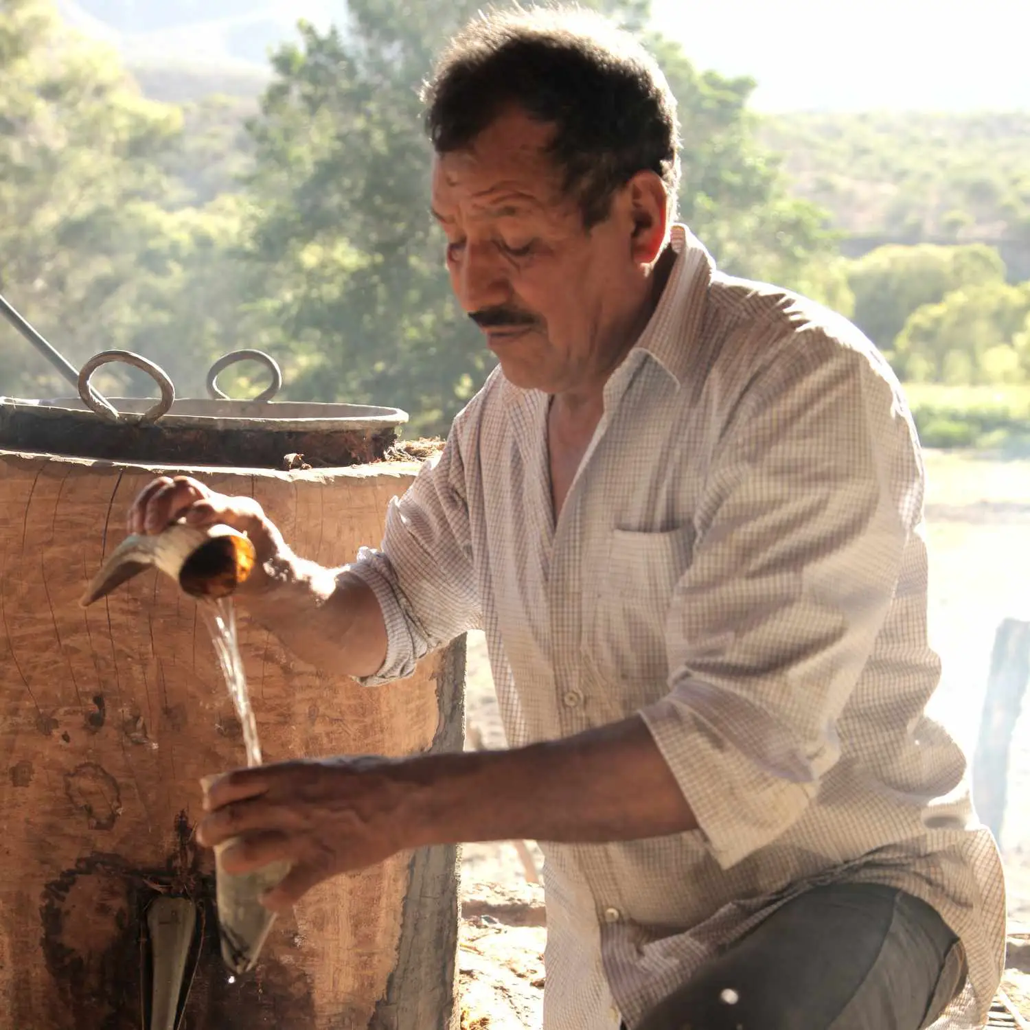 Man pouring mezcal next to a Filipino-style still