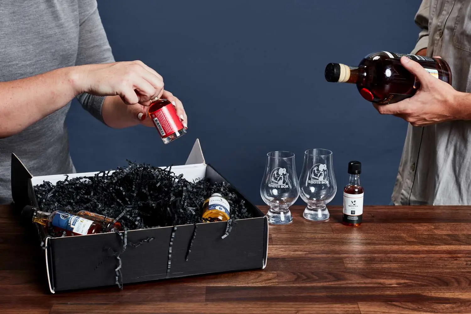 two people holding bottles of liquor next to a delivery box