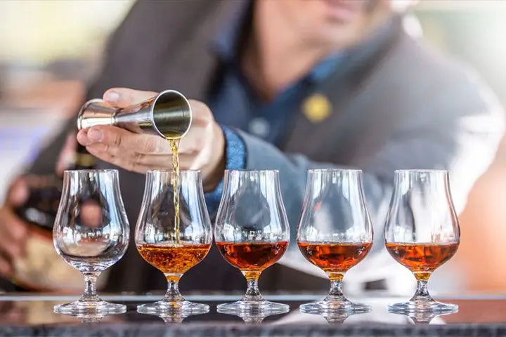A bartender pouring Armagnac into a row of tasting glasses from a jigger