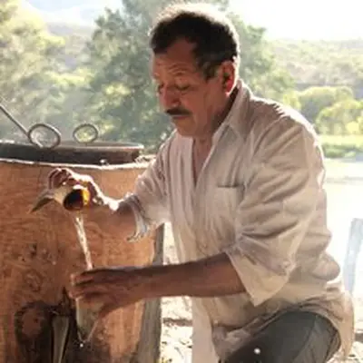 Man pouring mezcal next to a Filipino-style still