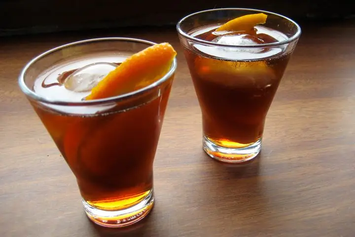 Two glasses of amber-hued homemade vermouth with ice and orange slices