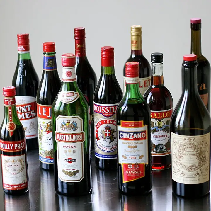 A group of 11 sweet vermouth bottles on a steel surface
