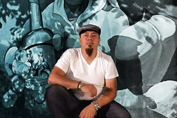 Mezcal expert Erick Rodriguez sits in front of a mezcal-themed grayscale mural