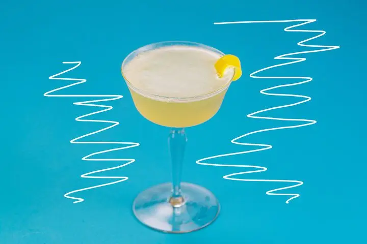 A shaken yellow cocktail served up in a wide coupe and garnished with lemon zest