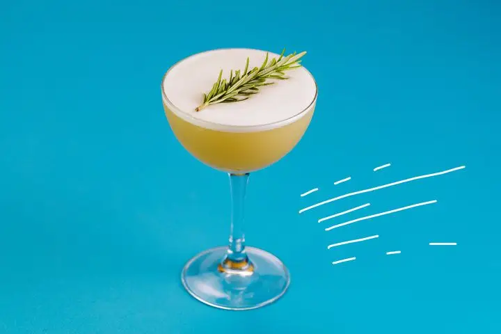 A soft yellow tequila sour served in a classic coupe and garnished with a sprig of rosemary